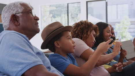 multi-generation african american family relaxing at home sitting on sofa watching tv together