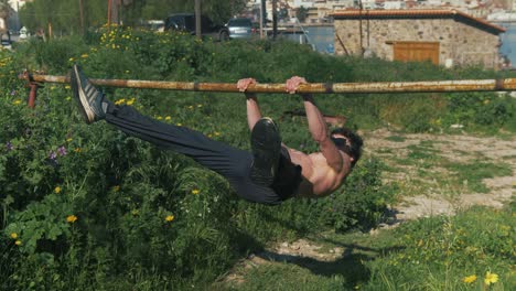 Athletic young male trains static straddle front lever gymnastic exercise outdoors shirtless
