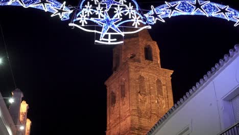 tiro inclinado en cámara lenta de un arco de entrada decorado para navidad con luces, copos de nieve brillantes y estrellas con vistas a la torre de una iglesia en medina sidonia en españa cádiz