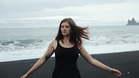 young beautiful woman in black dress dancing on black sand beach iceland, dramatic waves seascape, slow motion spinning