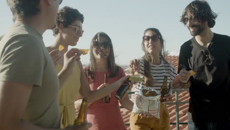 happy friends drinking beer and eating nachos at rooftop party on a summer day