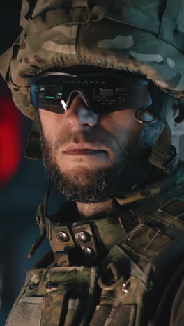 bearded military man in camouflage armor and hi tech goggles standing in illuminated passage during war. vertical shot