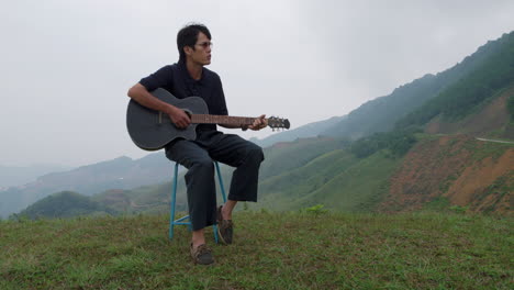 romantic asian guy playing guitar in slow motion on hilltop