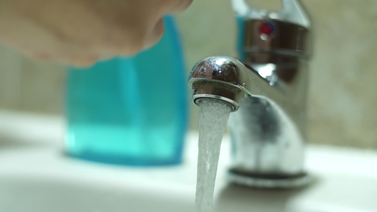 Person Washing Hands Under Running Water from Faucet