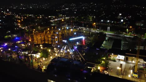 Vista-Nocturna-De-La-Ciudad-De-Medellin,-Pasando-Por-Un-Parque-De-Diversiones-En-El-Techo-De-Un-Centro-Comercial