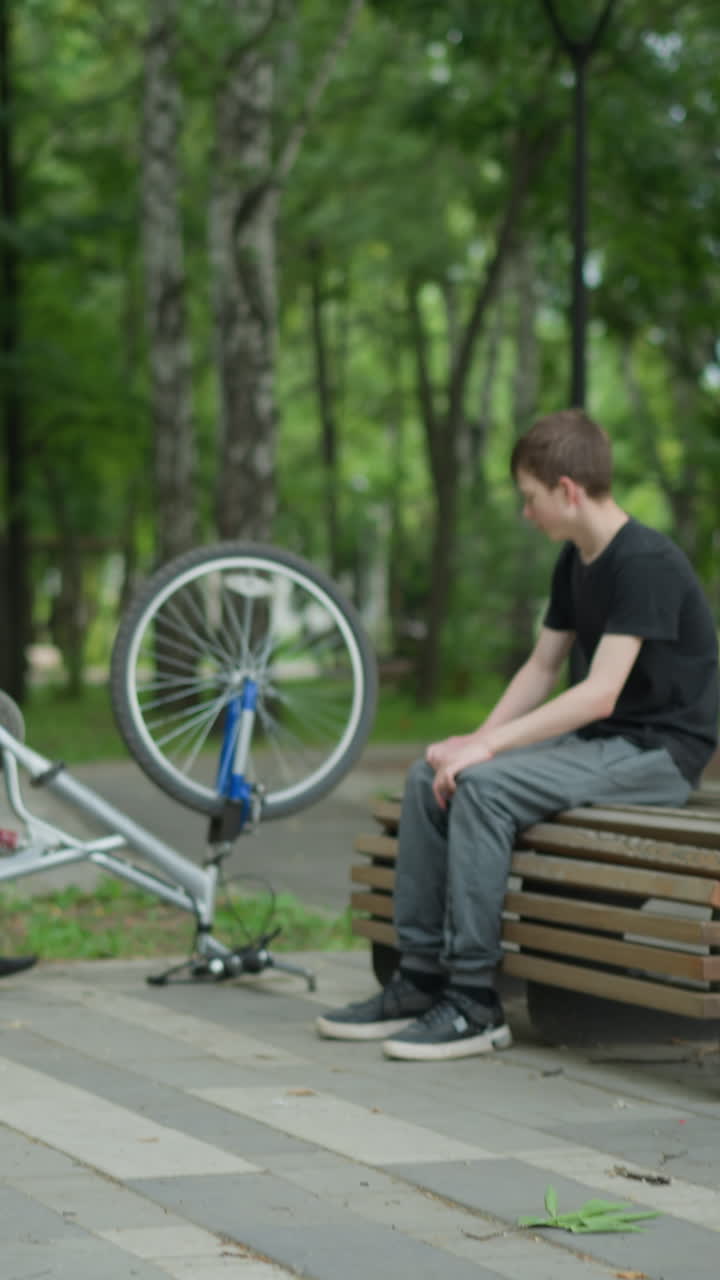 머리가 구부러진 어린 소년은 바 바 자전거 에 앉아 있으며, 다른 소년이 자전거를 타고 다가오고, 두 사람은 공원에서 대화하기 시작합니다.