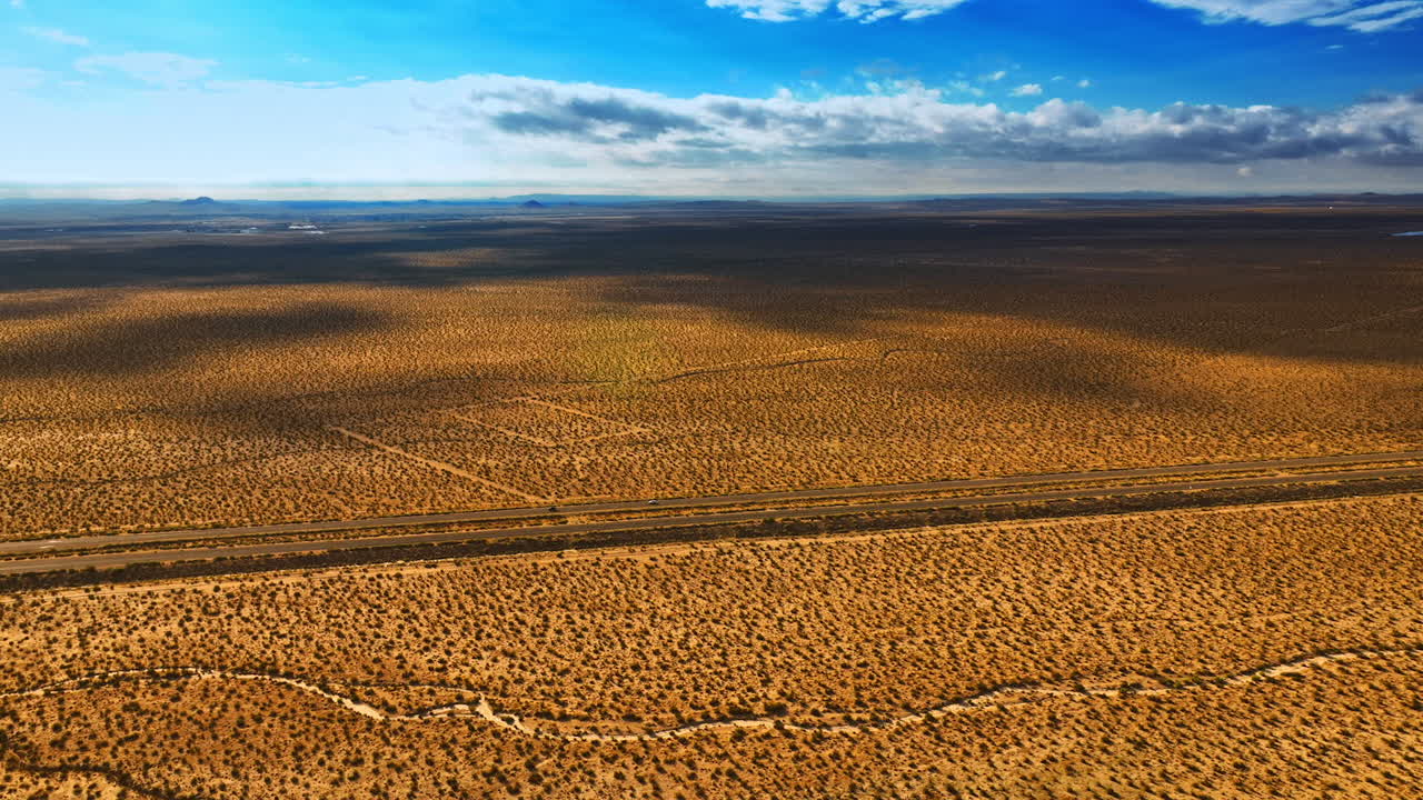 Endless scenery of the dry desert in California. Massive clouds shading the land from the sun. Cars run by the highway crossing the landscape. Top view.