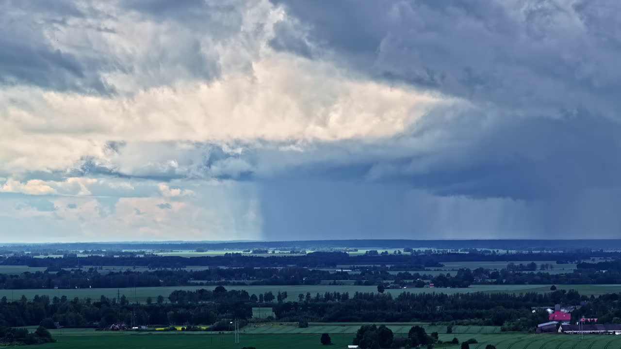 Aerial rising view reveals dark storm clouds sweeping over lush green fields and forests near Jelgava, Latvia, under dramatic skies