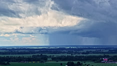 aerial rising view reveals dark storm clouds sweeping over lush green fields and forests near jelgava, latvia, under dramatic skies