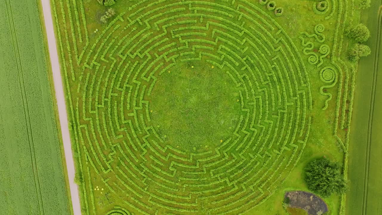 Vertical drone slowly rotating and moving closer over green maze field in Latvia