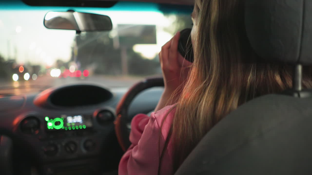 mujer conduciendo con una mano en el volante mientras bebe café con la otra, el fondo borroso muestra una carretera adelante con coches y semáforos en la distancia durante la noche