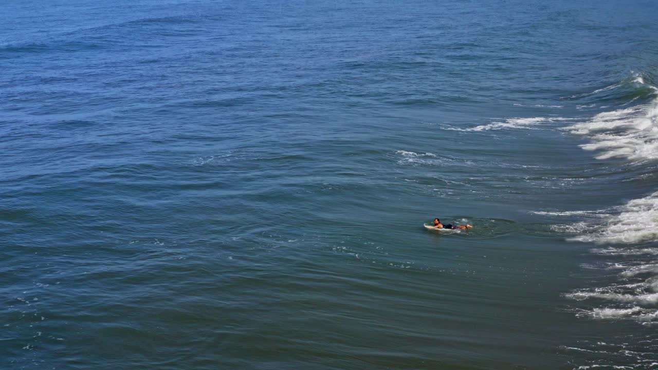 Surfer duck diving through breaking wave with surfboard, aerial view