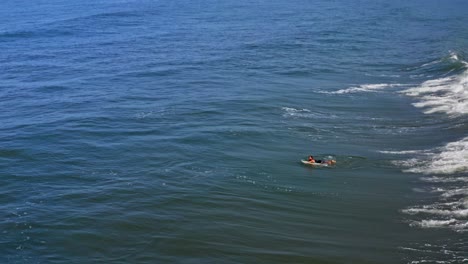 Surfer-duck-diving-through-breaking-wave-with-surfboard,-aerial-view