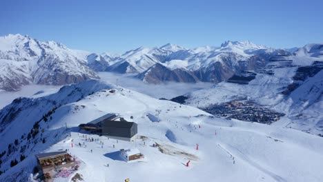 aerial 4k view of a ski resort with people skiing high up in the snow-capped mountains of the alps on a sunny day