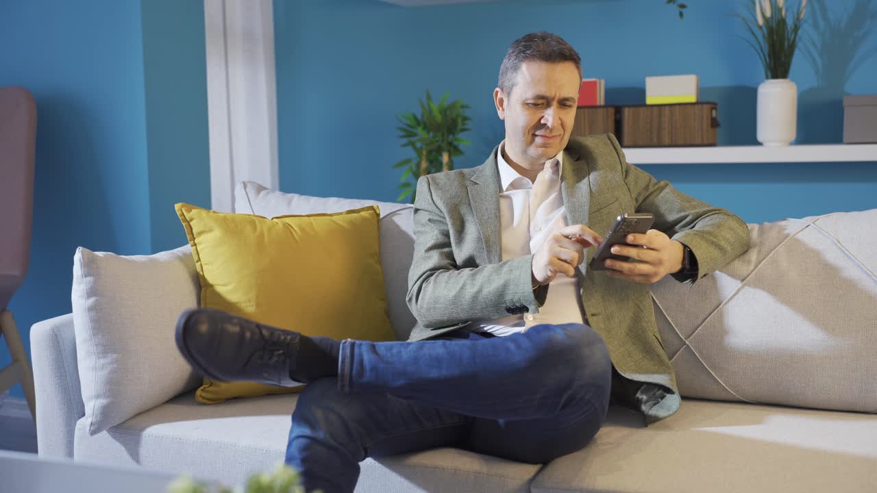 Mature man guy holding smartphone device sitting at home sending sms message.