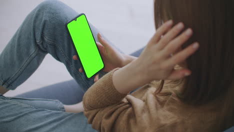 mujer en casa acostada en un sofá usando un teléfono inteligente con pantalla de maqueta verde haciendo gestos de desplazamiento de deslizamiento. hombre usando teléfono móvil internet redes sociales navegando. punto de vista de la cámara filmada