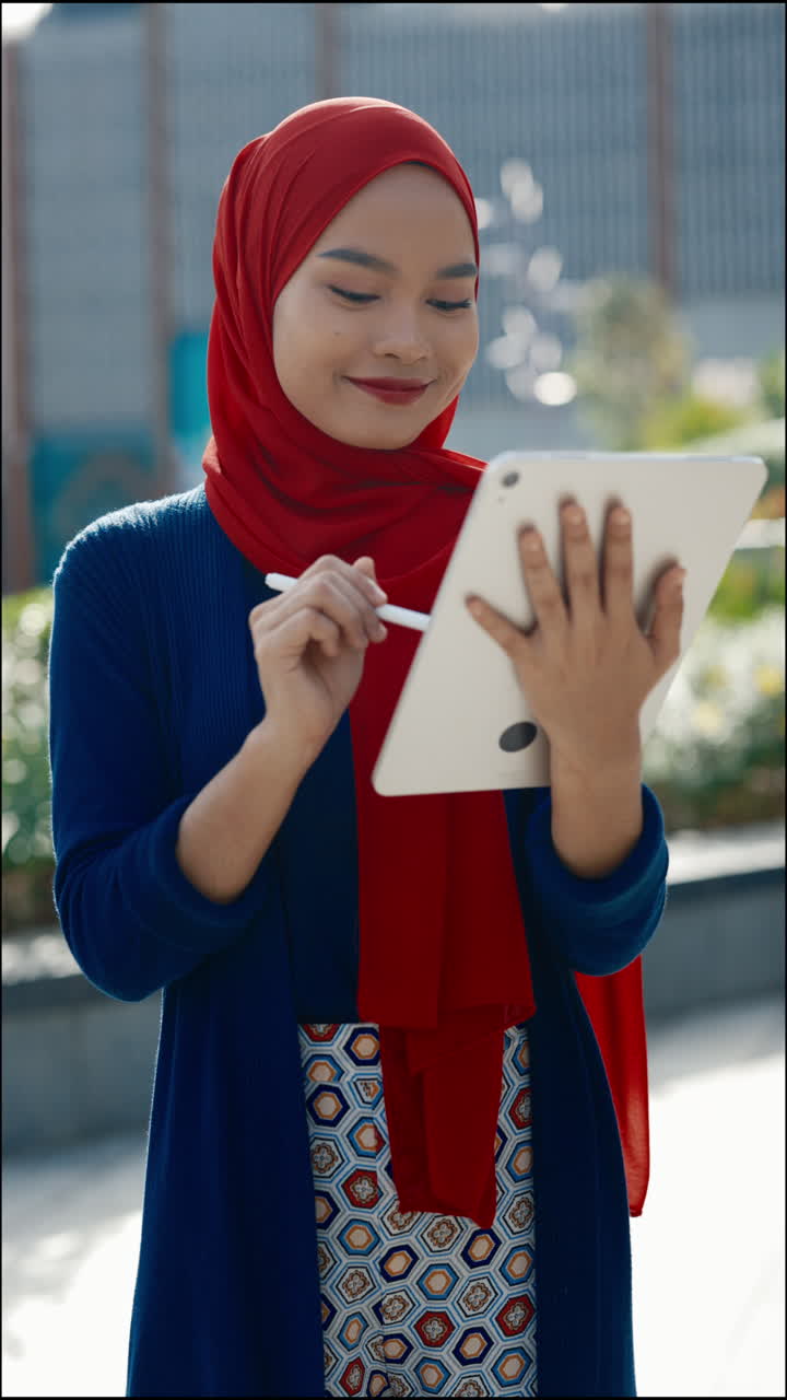 Young Woman in Hijab Using a Tablet and Stylus Outdoors