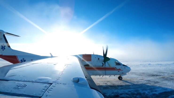 Een ambulancevliegtuig bereidt zich voor op het opstijgen op een besneeuwde landingsbaan, waarbij de medische noodcapaciteiten worden getoond onder een helderblauwe lucht tijdens winterse omstandigheden.