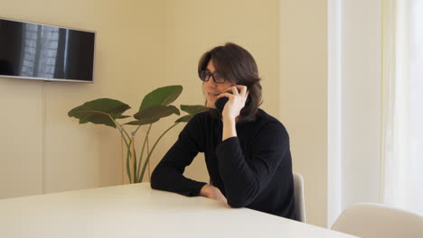 Young-man-with-glasses-talks-on-his-mobile-phone,-sitting-at-a-table