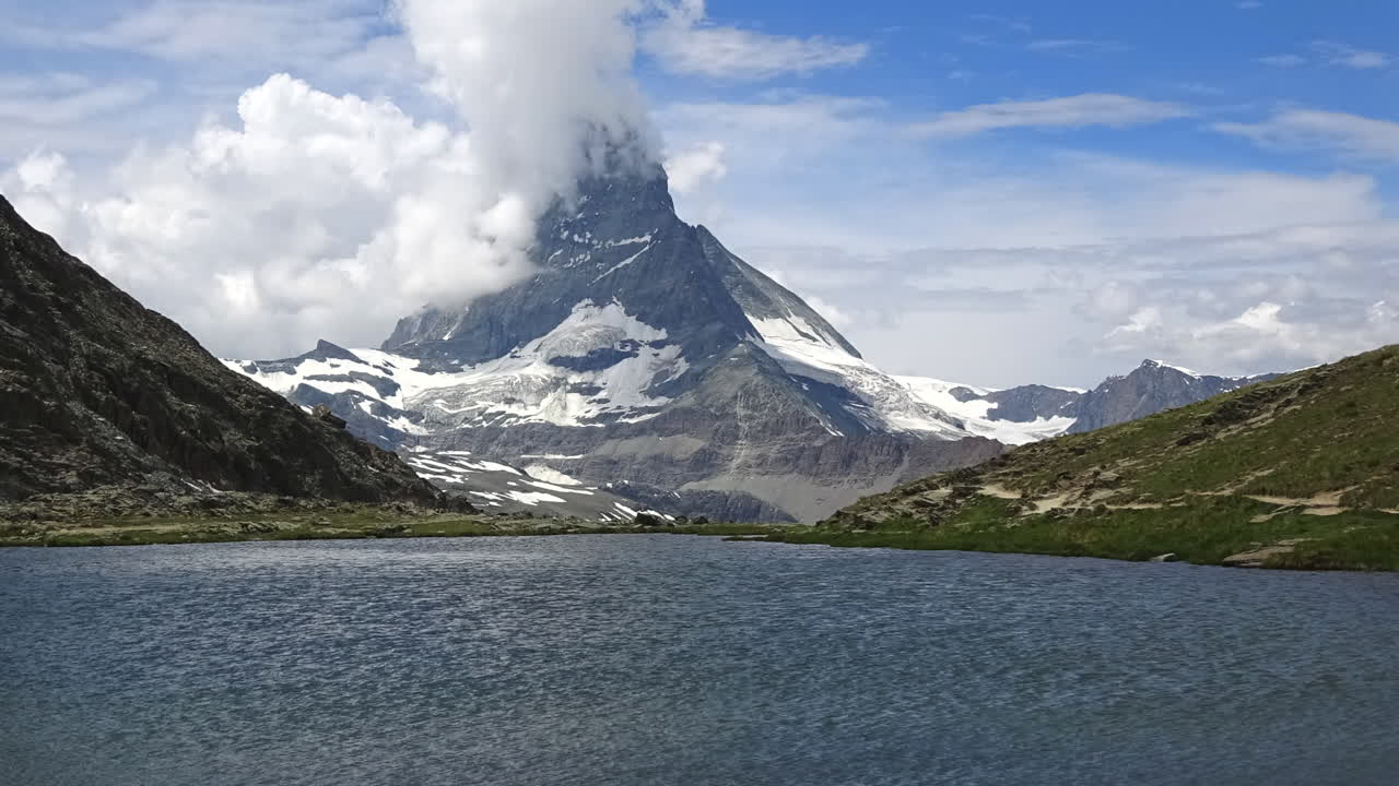 Filmato timelapse di nuvole che si muovono intorno al Cervino sopra un lago alpino calmo e pendii verdi a Zermatt, Vallese, Svizzera, suggestivo paesaggio montano estivo.