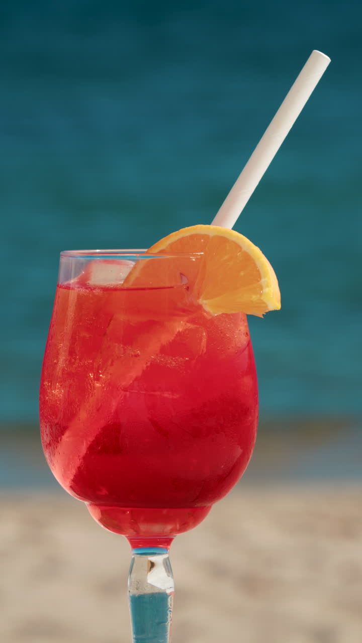 Close up of a refreshing red orange cocktail with orange slice and ice cubes, captured outdoors on a sunny day in Cannes. Vertical