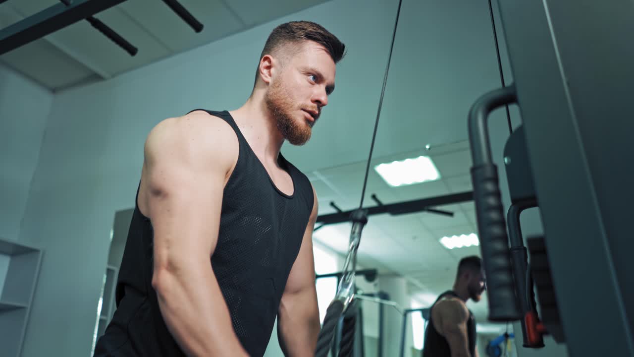 Side view of fit sportsman training his muscles. Muscular athlete is pulling rope on the modern simulator in sports center. Close-up.