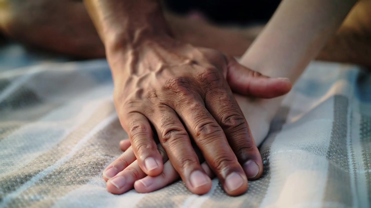 Due mani che si sovrappongono, sollevandosi, fluttuando e ritornando su una coperta a righe all'aperto, mostrando amore.