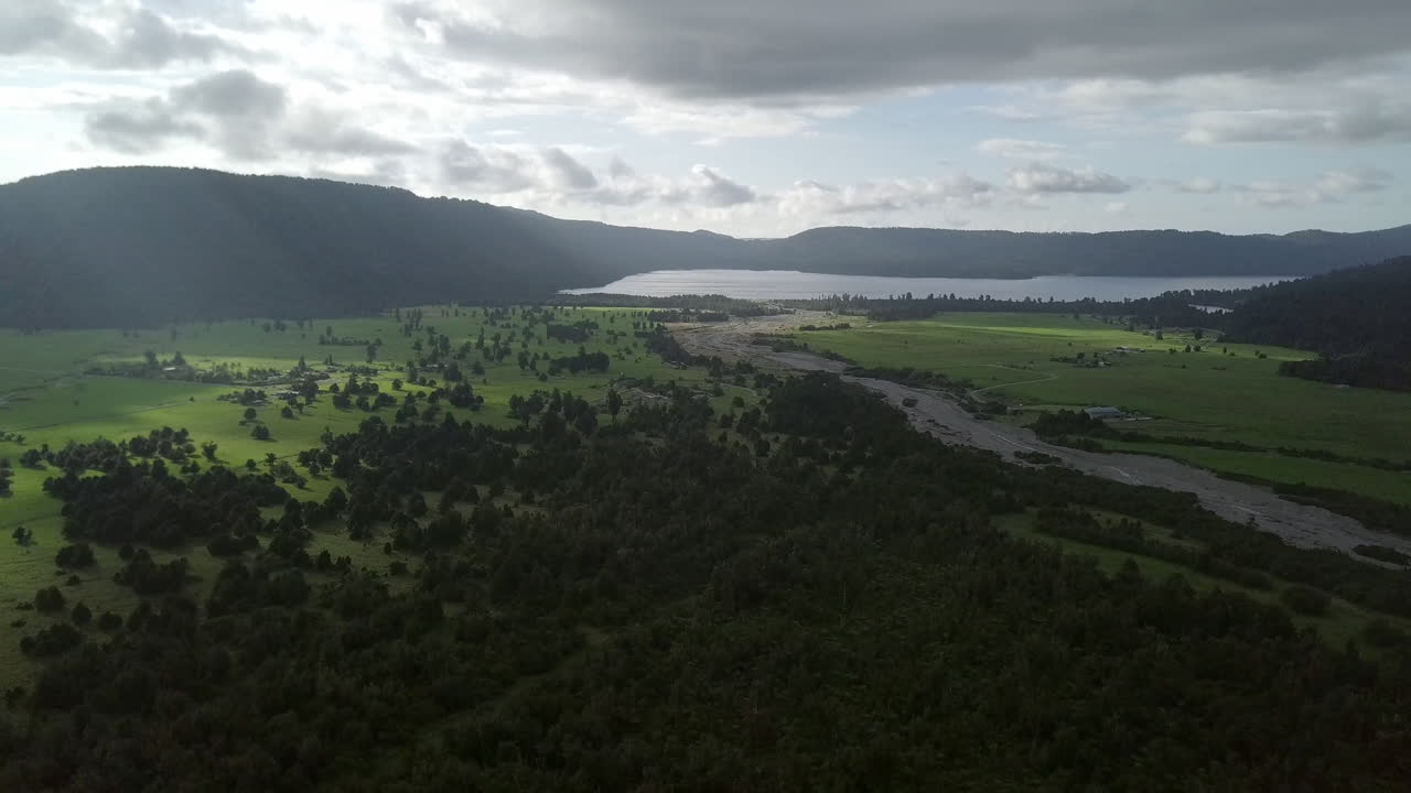 Aerial drone shot flying high above lush green farmland and mountains along the coast of New Zealand