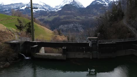 Una-Vista-Aérea-Captura-La-Presa-De-Un-Pequeño-Embalse-Ubicado-En-El-Pintoresco-Cañón-Del-Arroyo-Alpino-Fallbach,-Con-Vistas-Al-Lago-Walen,-Suiza