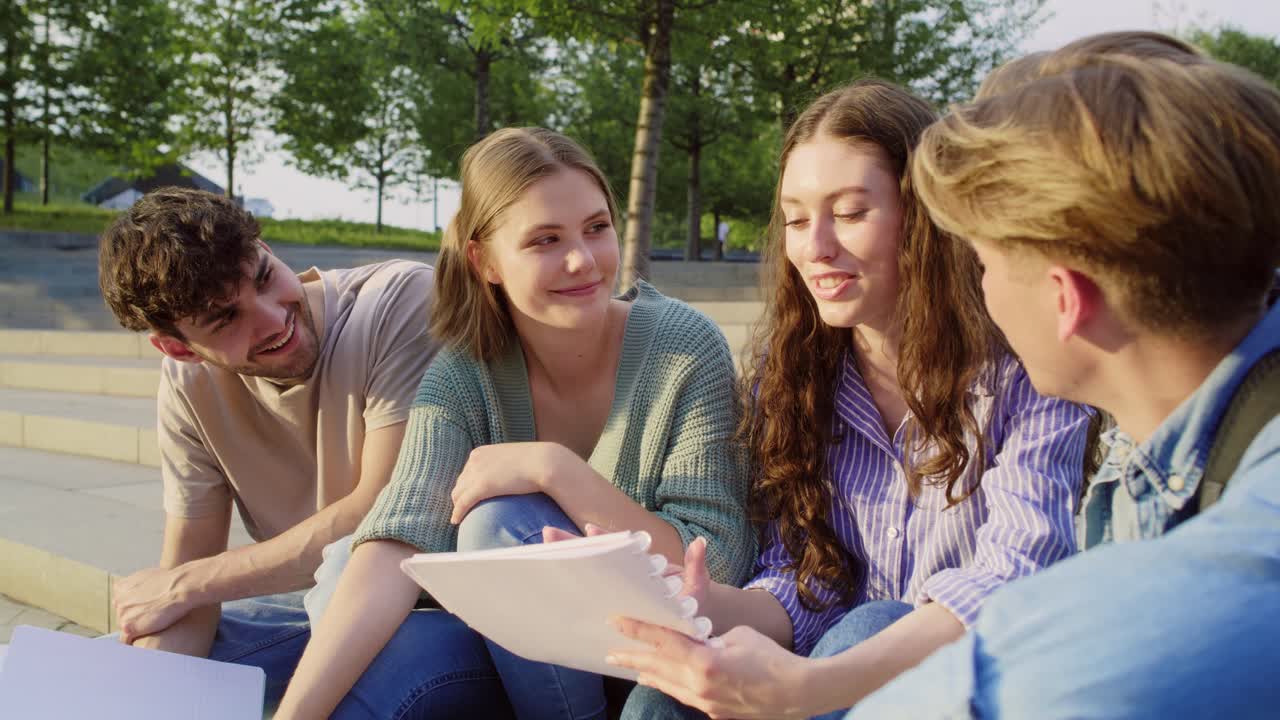 Gruppe kaukasiske studenter som leser til eksamen mens de sitter utenfor universitetsområdet