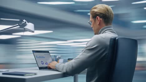 360 degree modern office: handsome businessman sitting at his desk working on a laptop computer. man working with big data e-commerce analysis. energetic fast tracking shot. camera moving around