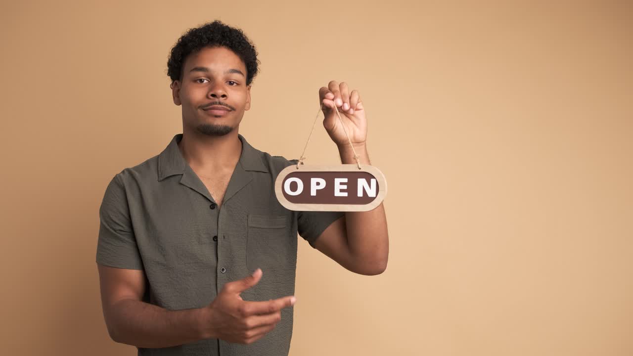 Smiling man with open sign inviting in beige studio