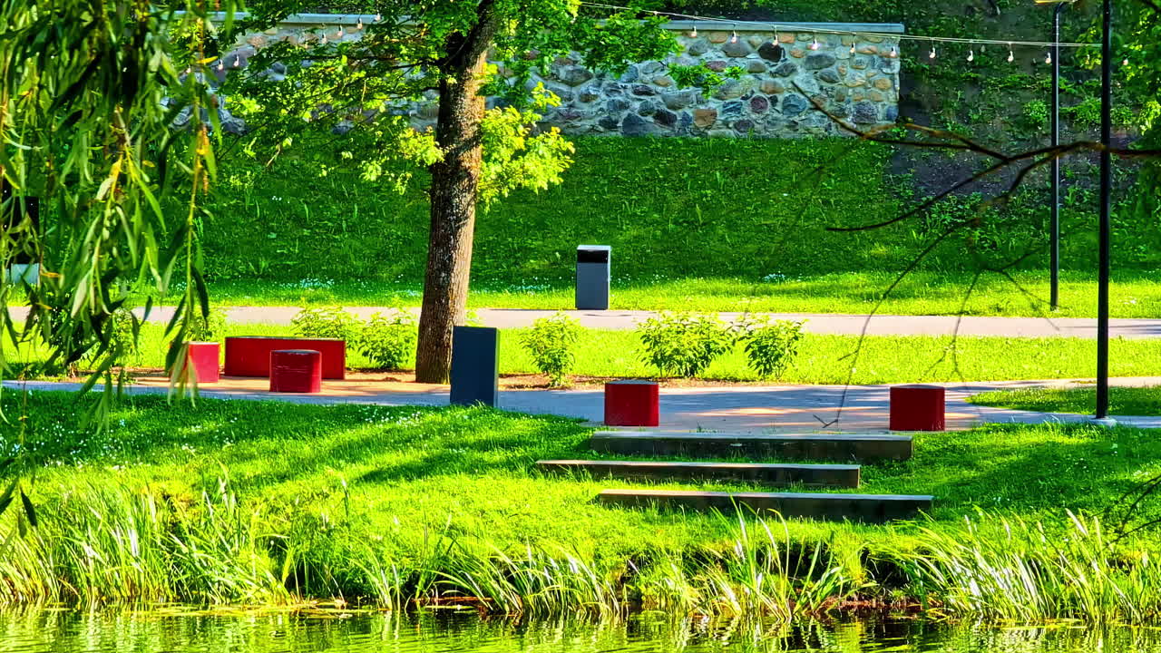 Bright city park with green grass red benches and stone wall during sunny summer day