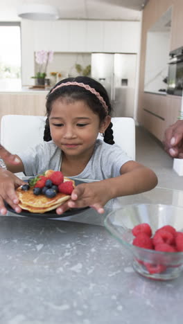 vertical video: eating pancakes with berries, girl enjoying breakfast at home kitchen table