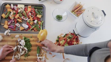 una feliz pareja de lesbianas caucásicas preparando comida y usando una tableta en una cocina soleada