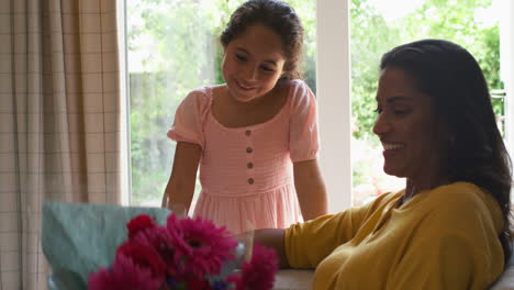 daughter giving mother bunch of flowers and homemade card for birthday or mothers day at home