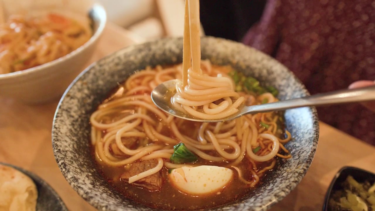 Primo piano di bacchette che sollevano noodles da una ciotola di zuppa di manzo piccante a Bangkok