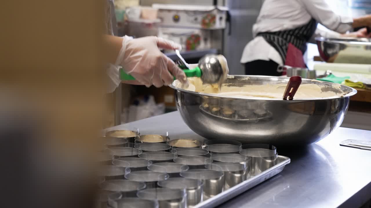 Baker uses ice cream scoop to portion out cupcake batter into round rings, slow motion 4K