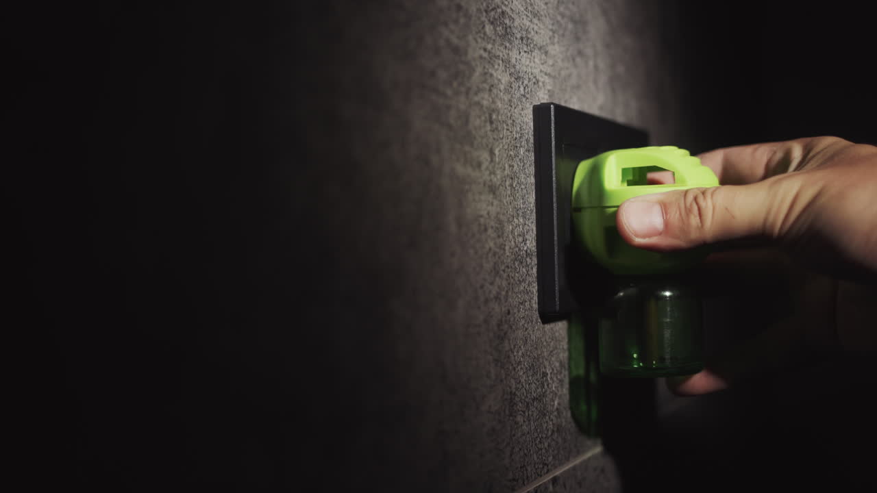 A man's hand inserts an electric fumigator into a socket on the wall