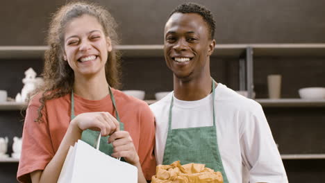 close up view of two co workers at a pottery store posing in front of the camera while smiling and hugging each other 1