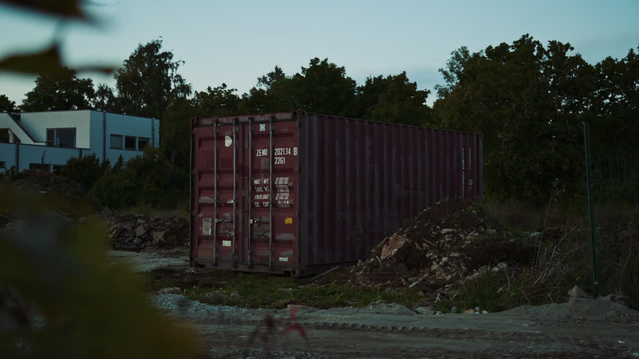 Brown shipping container with white text standing at the side of dirt road