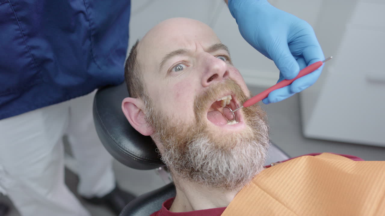Man with dentophobia opens mouth and dentist inserts forceps, funny expression