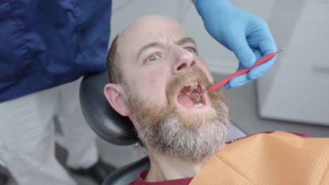 man with dentophobia opens mouth and dentist inserts forceps, funny expression