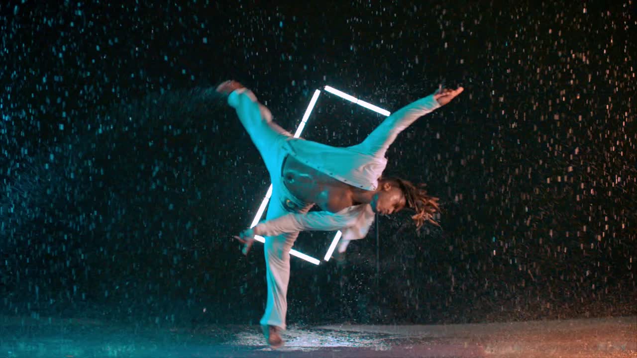 Capoeira dancer performing amazing spinning jump in the rain in super slow motion