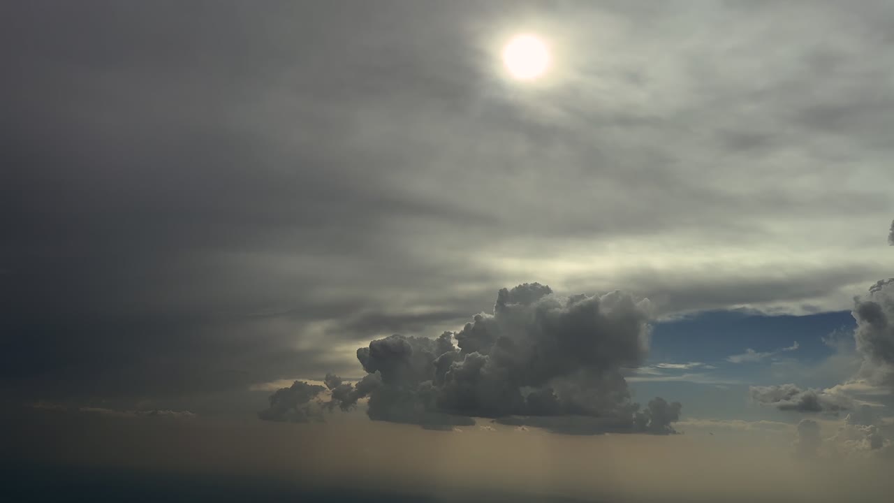 An immervive pilot’s view from inside a jet cockpit flying through a stormy sky with some threatening storm clouds and the sun veiled by a layer of ethereal clouds. 4K