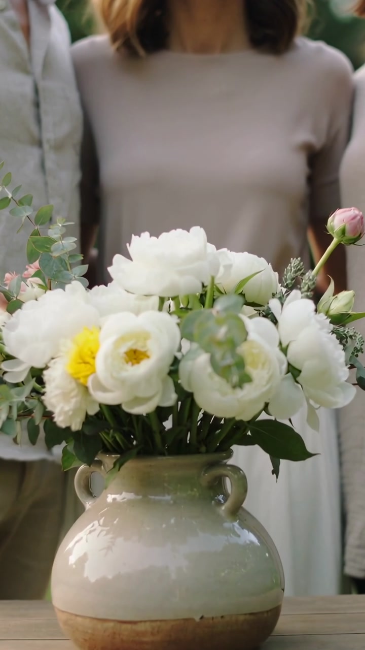 Vertical video: Shifting vase bouquet during subtle zoom at patio table, center beige, three posing