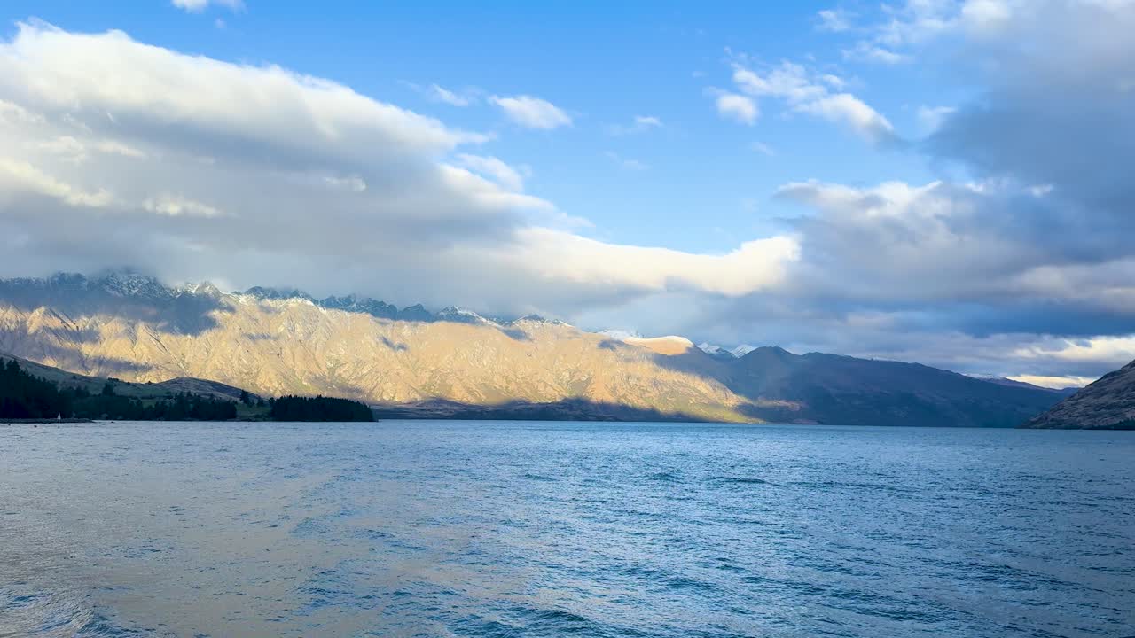 A tranquil lake with majestic mountains under a dynamic sky, captured in natural lighting with gentle camera movement