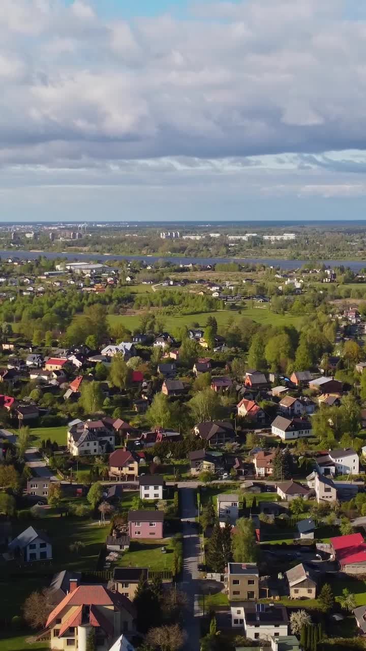 Verticale di un'area suburbana con strade che si intersecano e una leggera vegetazione primaverile, in movimento verso sinistra con fiume e fabbriche in lontananza