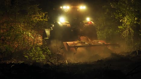 forestry mulcher creates cloud of dust when working in the forest at night