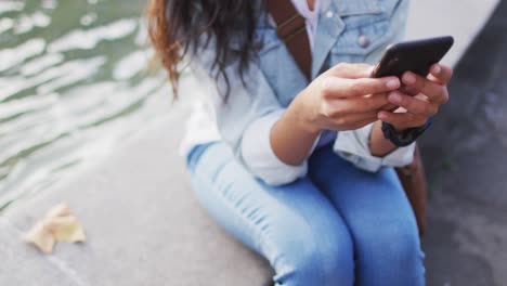 mujer asiática sentada al lado de la fuente usando un teléfono inteligente